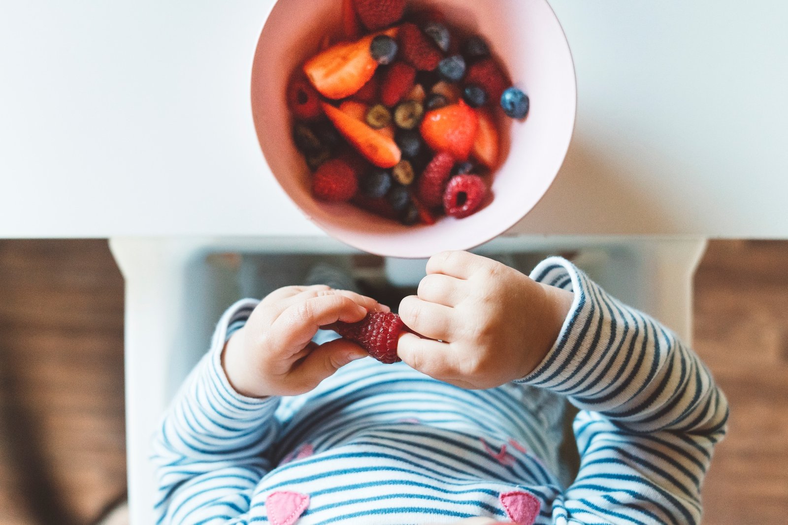 The baby is trying a new taste of solid food. Eating healthy food from the beginning is important. Y